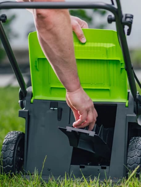 מכסחת דשא 41 ס״מ (16 אינץ׳) 48 וולט נטענת נדחפת, Greenworks LM4102: תקריב של הדש האחורי מורם ויד שמכניסה את פקק הריסוק לפתח הפליטה
