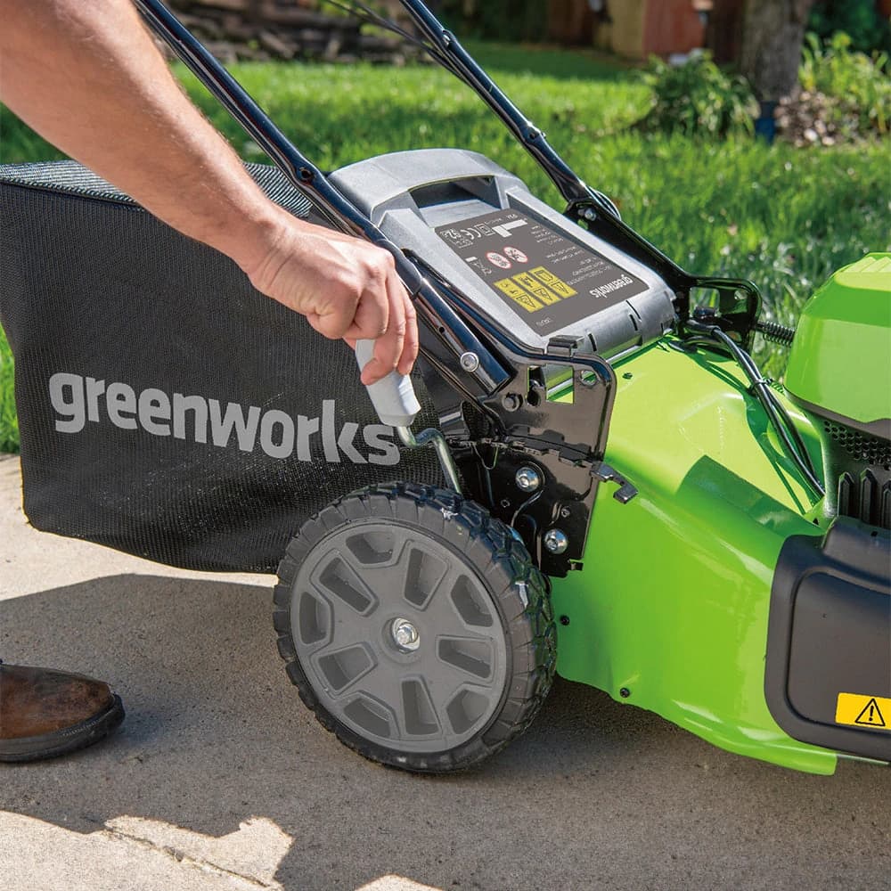 מכסחת דשא 46 ס״מ 48 וולט נטענת נסיעה עצמית, Greenworks GD24X2LM46SP: תקריב של כוונון גובה החיתוך בידית שליד הגלגל האחורי, עם שק האיסוף מחובר