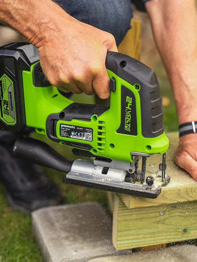 מסור אנכי 24 וולט נטען, Greenworks GD24JS: תקריב של ניסור קורת עץ בחוץ, הסוללה מחוברת