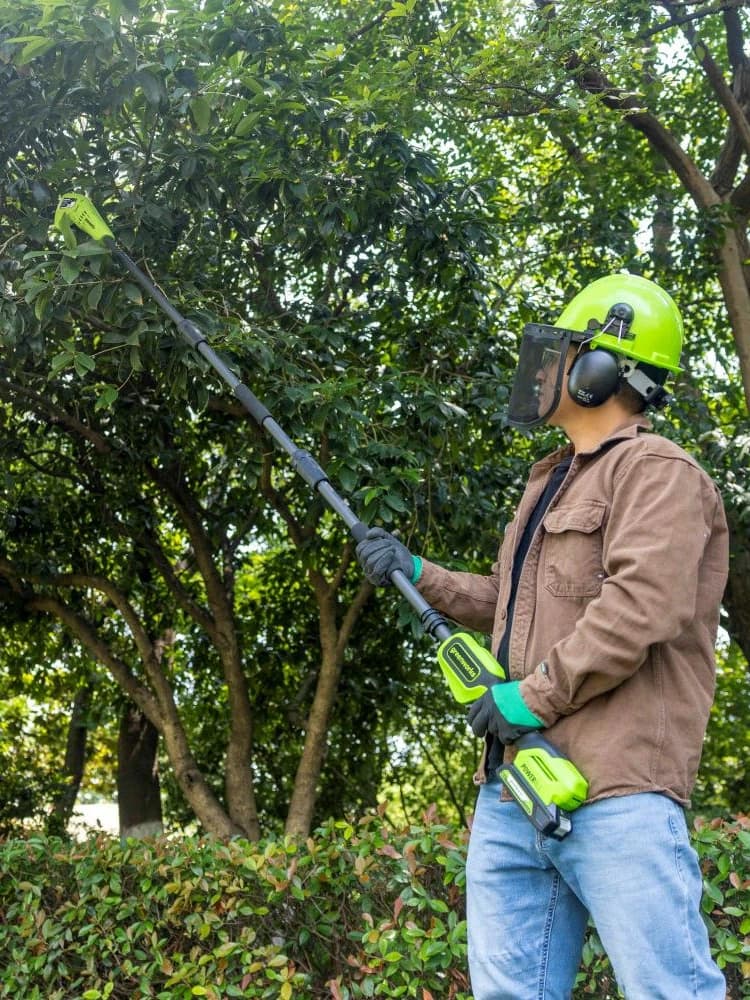 מסור גבהים 20 ס״מ 24 וולט נטען דור 2 גוף בלבד, Greenworks PS24B00-01: אדם עם קסדה ומגן פנים מנסר ענף גבוה בעץ, בעמידה על הקרקע